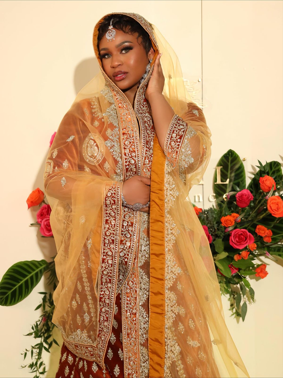 Jessica Divine in a saffron and gold embroidered gown with a veil, beside a bouquet of red and orange roses